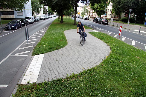 Radfahrender auf dem befestigten Weg eines Mittelstreifens einer Straße mit zwei getrennten Fahrspuren